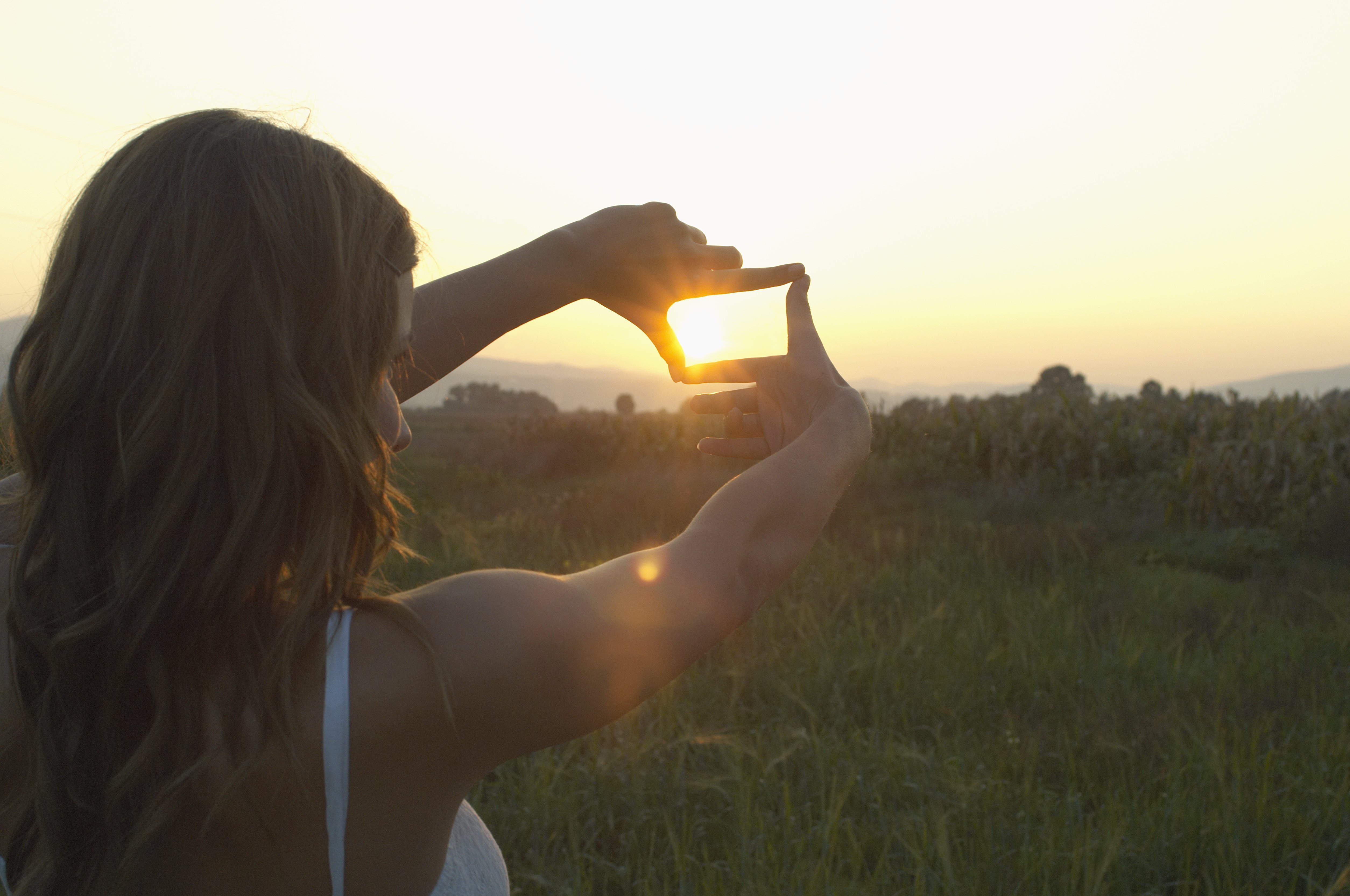 Teenage girl (16-18) outdoors, framing sun with fingers